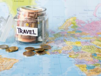Travel budget concept. Money saved for vacation in glass jar on map background
